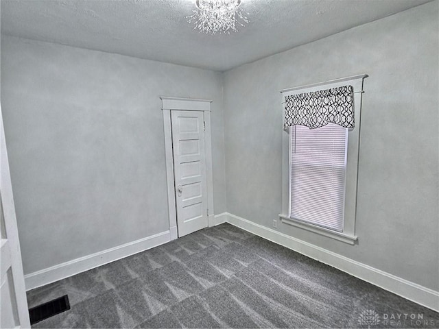 spare room featuring baseboards, visible vents, dark colored carpet, a textured ceiling, and a notable chandelier