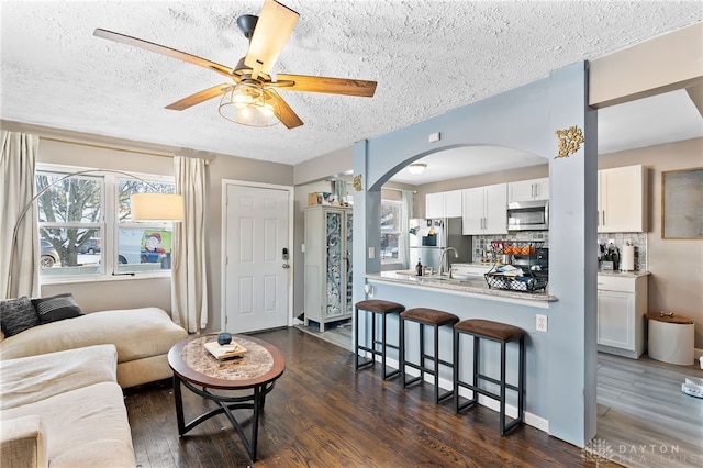 living room featuring arched walkways, ceiling fan, a textured ceiling, and dark wood finished floors