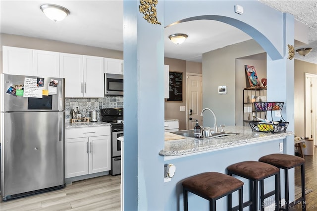 kitchen featuring stainless steel appliances, a peninsula, a sink, white cabinetry, and light stone countertops