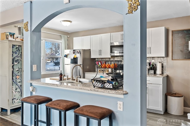 kitchen featuring arched walkways, light stone counters, stainless steel appliances, a sink, and white cabinetry