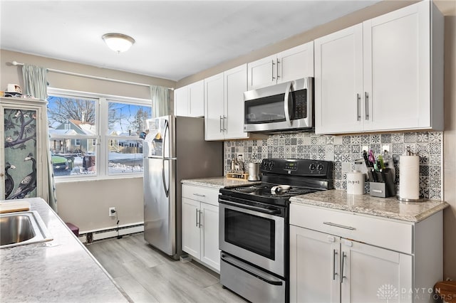 kitchen featuring light stone counters, white cabinetry, appliances with stainless steel finishes, baseboard heating, and backsplash