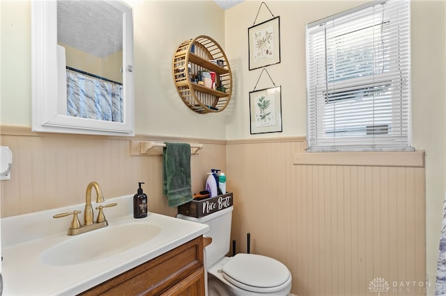 full bathroom featuring toilet, a wainscoted wall, and vanity