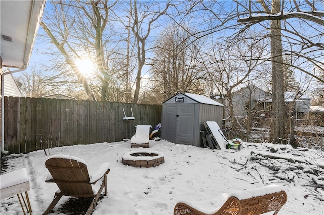 yard layered in snow featuring a fire pit, a shed, an outbuilding, and a fenced backyard