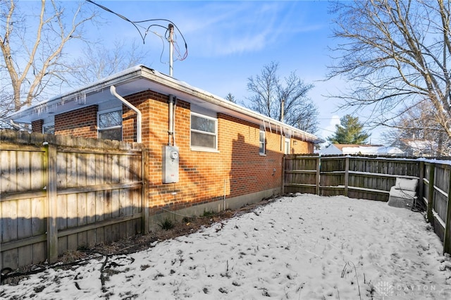 view of snow covered exterior featuring fence and brick siding