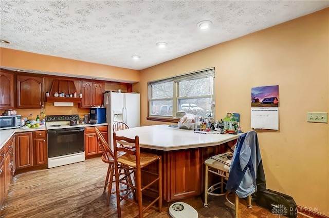 kitchen featuring light countertops, light wood-style floors, white appliances, a peninsula, and a kitchen bar