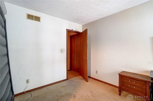 unfurnished room with a textured ceiling, light colored carpet, visible vents, and baseboards