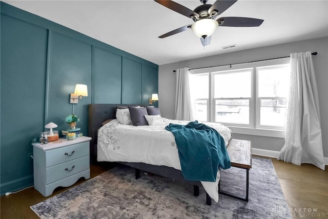 bedroom with ceiling fan, visible vents, a decorative wall, and dark wood finished floors