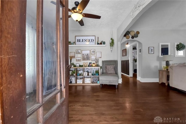 sitting room featuring arched walkways, ceiling fan, a textured ceiling, dark wood-style flooring, and baseboards