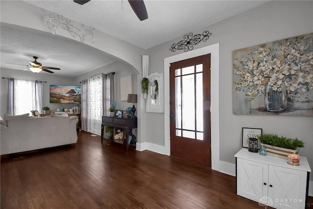 entryway featuring baseboards, arched walkways, dark wood finished floors, a ceiling fan, and a textured ceiling