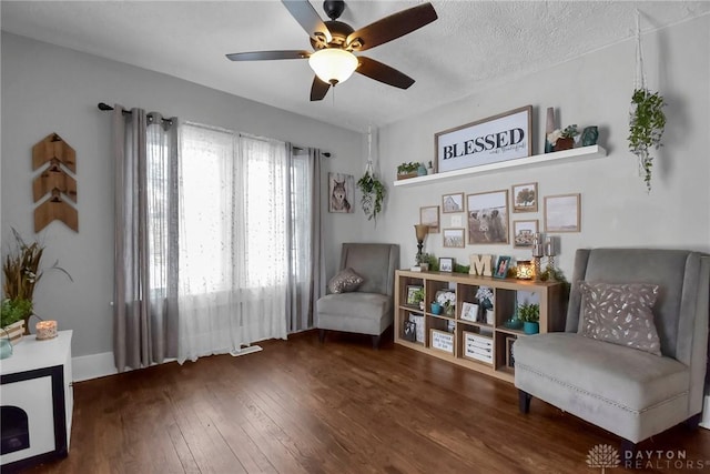 living area featuring dark wood-type flooring, a textured ceiling, and a ceiling fan