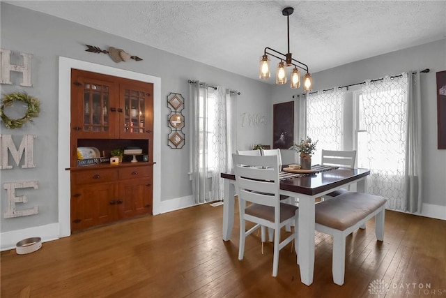 dining room featuring a textured ceiling, baseboards, dark wood finished floors, and an inviting chandelier