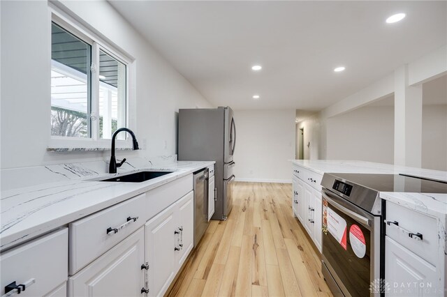 kitchen with light stone counters, white cabinetry, stainless steel appliances, and a sink