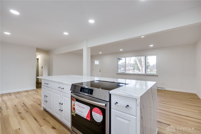 kitchen with stainless steel range with electric stovetop, white cabinets, light wood finished floors, and a center island