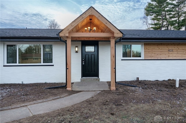 doorway to property with brick siding and a shingled roof