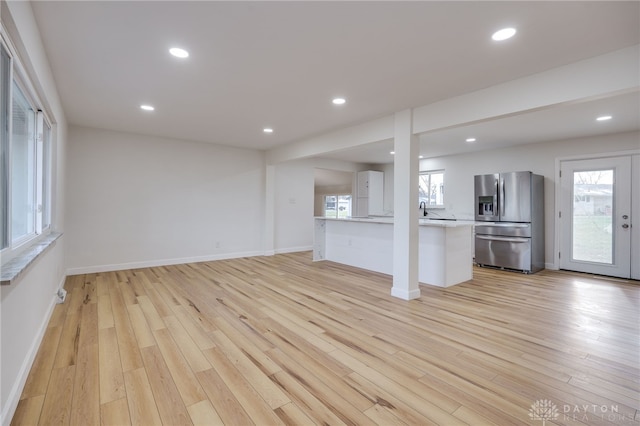 unfurnished living room featuring baseboards, light wood-type flooring, a sink, and recessed lighting