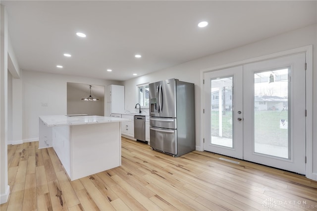 kitchen featuring a sink, a kitchen island, white cabinets, appliances with stainless steel finishes, and pendant lighting