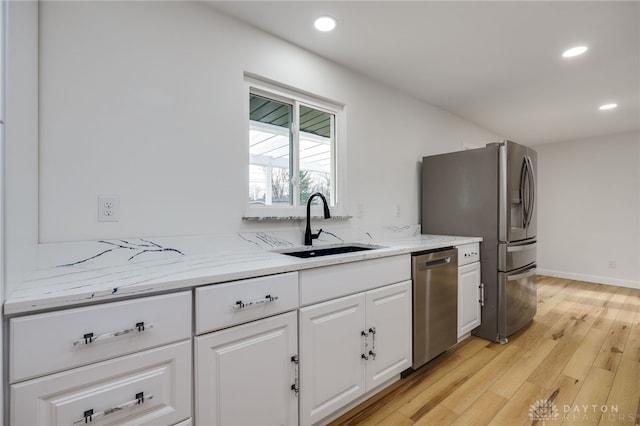 kitchen with appliances with stainless steel finishes, white cabinetry, a sink, and light stone counters