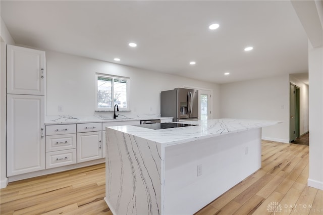 kitchen featuring light wood finished floors, a kitchen island, white cabinetry, stainless steel refrigerator with ice dispenser, and a sink