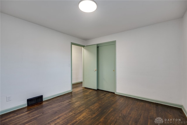 unfurnished bedroom with baseboards, visible vents, dark wood finished floors, and a closet