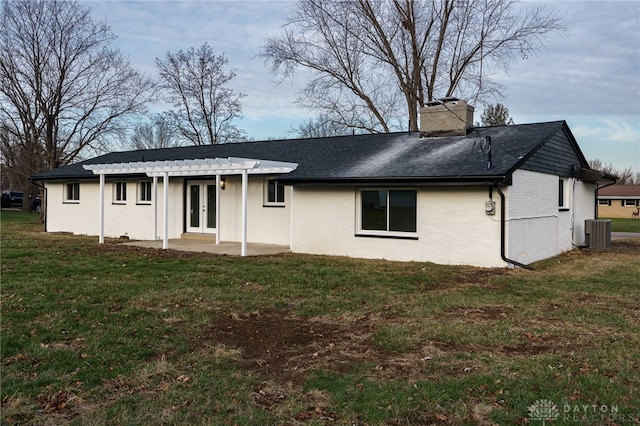 view of front of house with cooling unit, brick siding, a chimney, and a front lawn