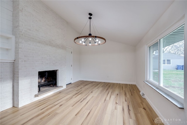 unfurnished living room featuring light wood finished floors, baseboards, lofted ceiling, a fireplace, and a notable chandelier