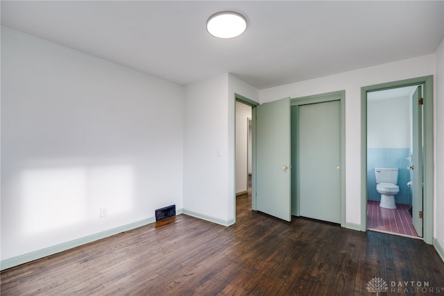 unfurnished bedroom with baseboards, tile walls, ensuite bath, dark wood-style flooring, and a closet