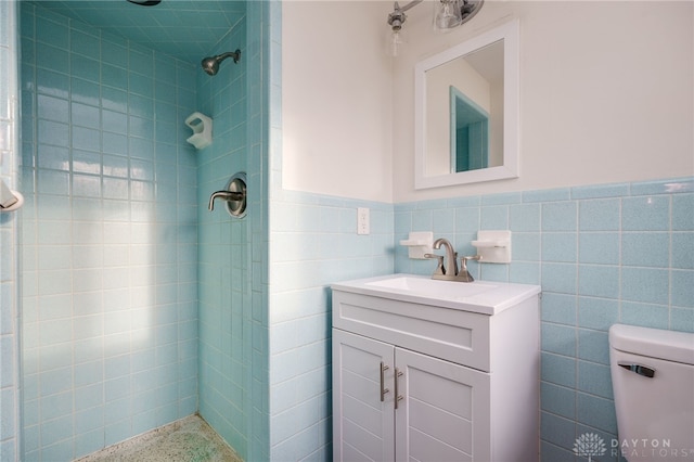 bathroom featuring vanity, tile walls, tiled shower, and wainscoting