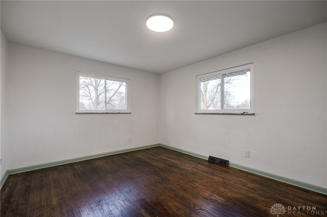 unfurnished room featuring dark wood-type flooring, visible vents, and baseboards