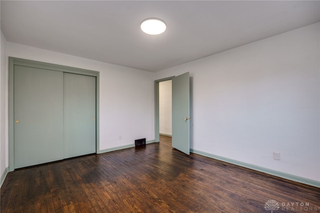 unfurnished bedroom with a closet, visible vents, dark wood finished floors, and baseboards