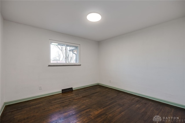 empty room with dark wood-type flooring, visible vents, and baseboards