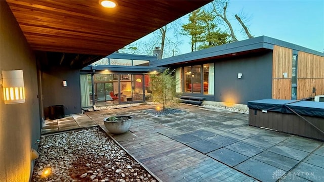 back of house at dusk featuring a patio area and a hot tub