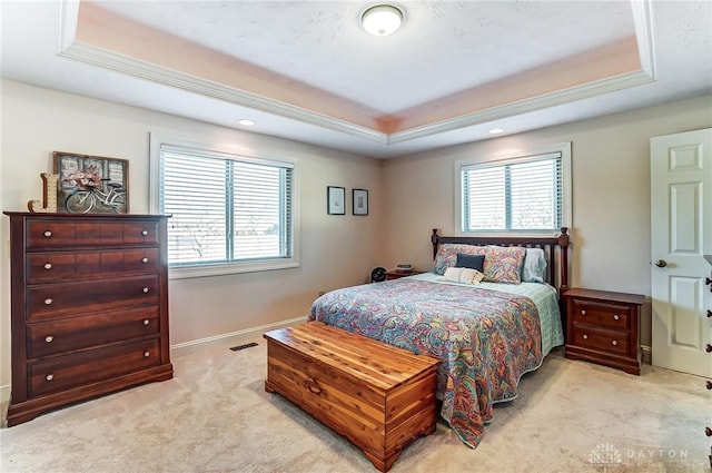 bedroom featuring a tray ceiling, light carpet, visible vents, and baseboards