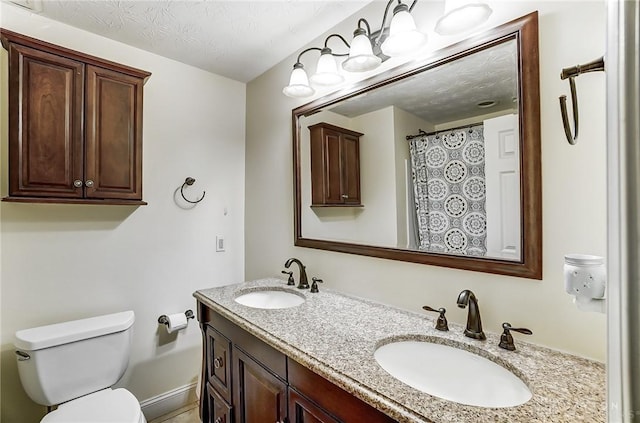 bathroom featuring a textured ceiling, double vanity, a sink, and toilet