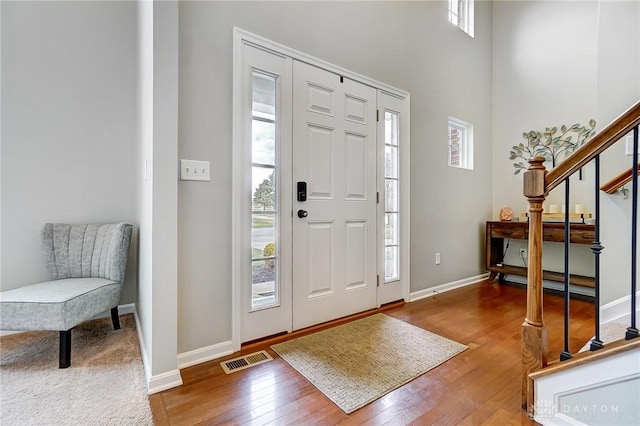 entryway featuring wood-type flooring, visible vents, a towering ceiling, stairway, and baseboards