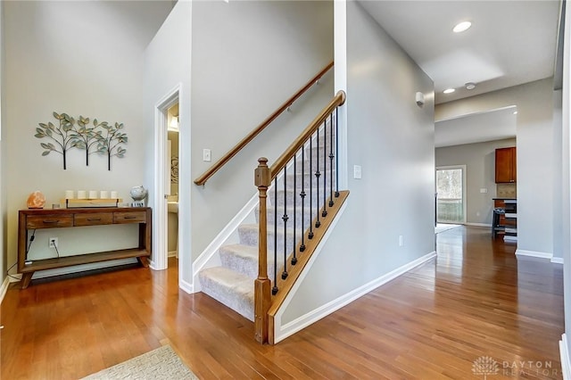 stairway with recessed lighting, wood finished floors, a towering ceiling, and baseboards