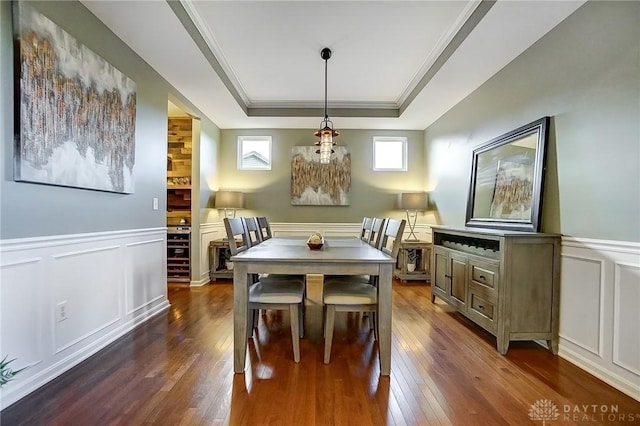 dining space featuring a tray ceiling, dark wood-style flooring, a wainscoted wall, crown molding, and a decorative wall