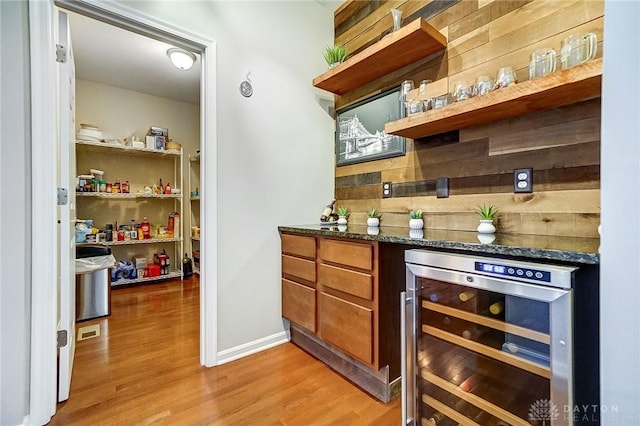 bar with a bar, wine cooler, wood finished floors, and baseboards