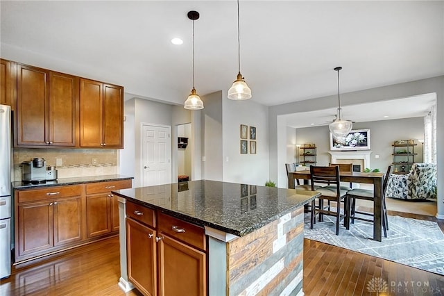 kitchen with brown cabinetry, dark stone counters, pendant lighting, and a center island