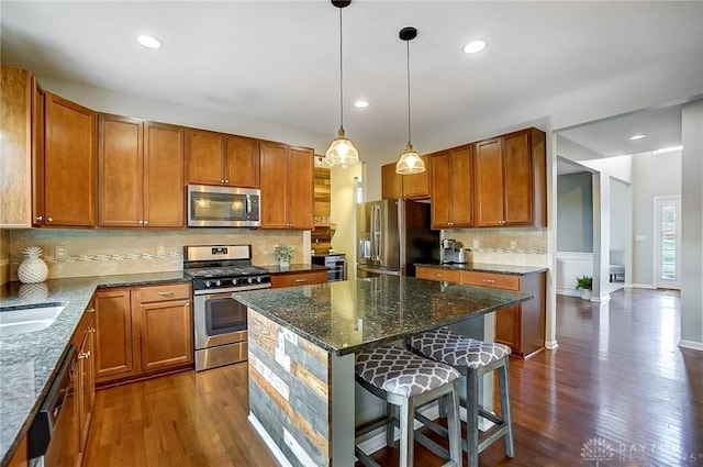 kitchen with brown cabinetry, a kitchen island, a kitchen breakfast bar, dark stone countertops, and stainless steel appliances