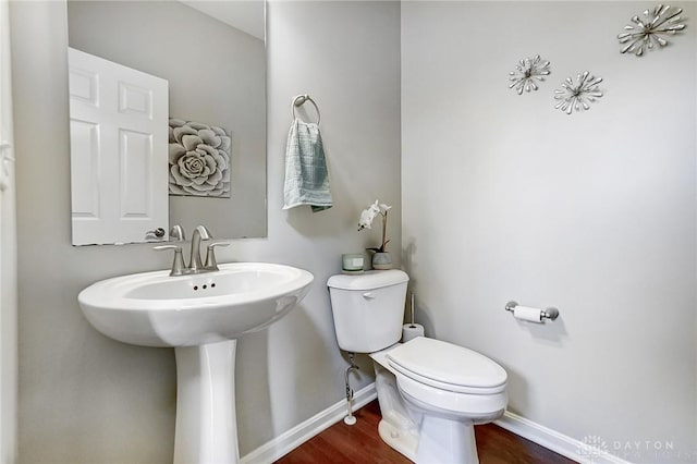 half bathroom with toilet, baseboards, and wood finished floors