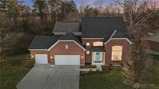 view of front facade with fence, roof with shingles, concrete driveway, a garage, and brick siding