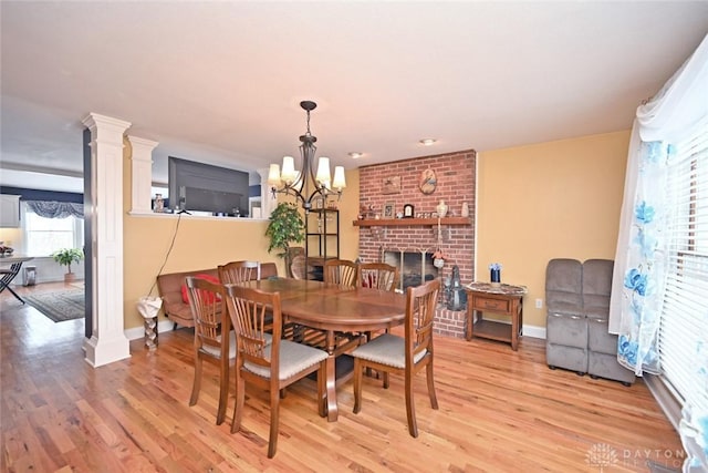 dining space featuring light wood-type flooring, a brick fireplace, decorative columns, and baseboards