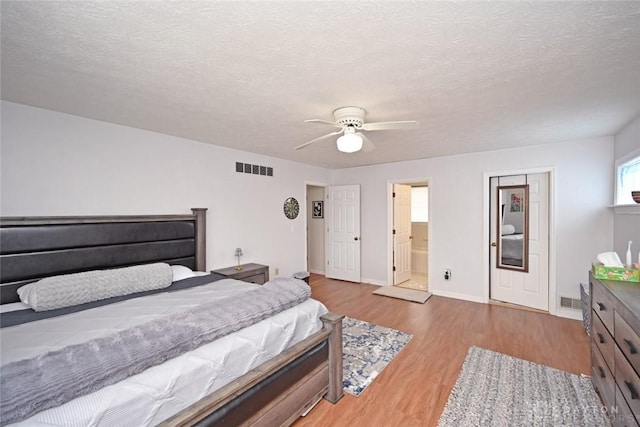 bedroom featuring light wood-type flooring, baseboards, visible vents, and a textured ceiling