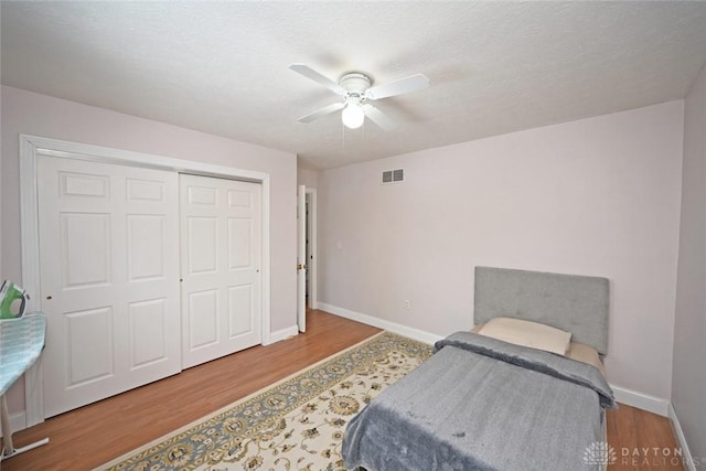 bedroom featuring wood finished floors, a ceiling fan, visible vents, baseboards, and a closet