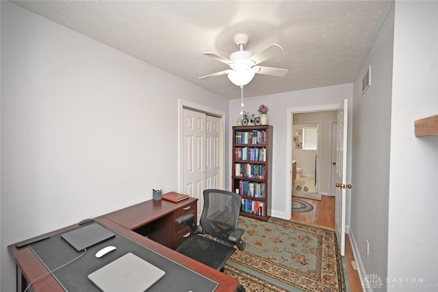 office area featuring ceiling fan, a textured ceiling, wood finished floors, visible vents, and baseboards