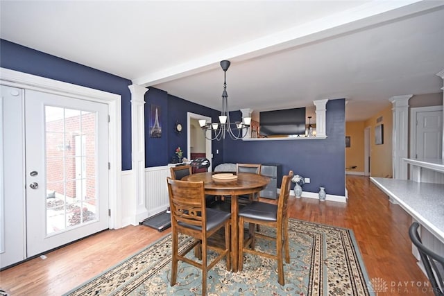 dining room with wainscoting, decorative columns, an inviting chandelier, and wood finished floors