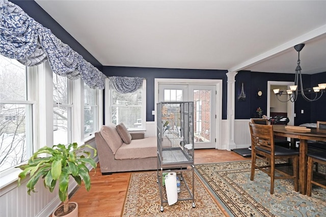 interior space featuring french doors, decorative columns, wainscoting, wood finished floors, and a chandelier