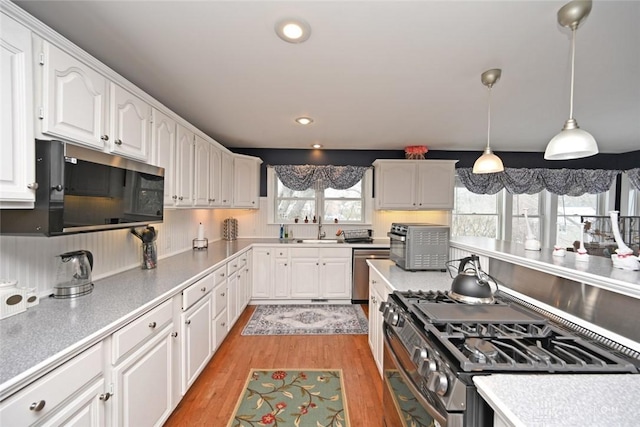 kitchen featuring white cabinets, light wood-style flooring, stainless steel appliances, light countertops, and pendant lighting