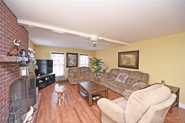 living area featuring light wood finished floors, ceiling fan, a fireplace, and beamed ceiling