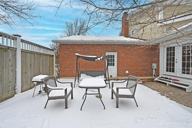 snow covered patio featuring fence and french doors